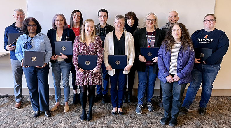 A dozen people stand against a white background and smile.