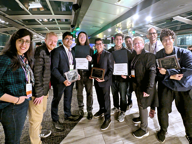 Ten people stand in a half circle holding certificates and smile.