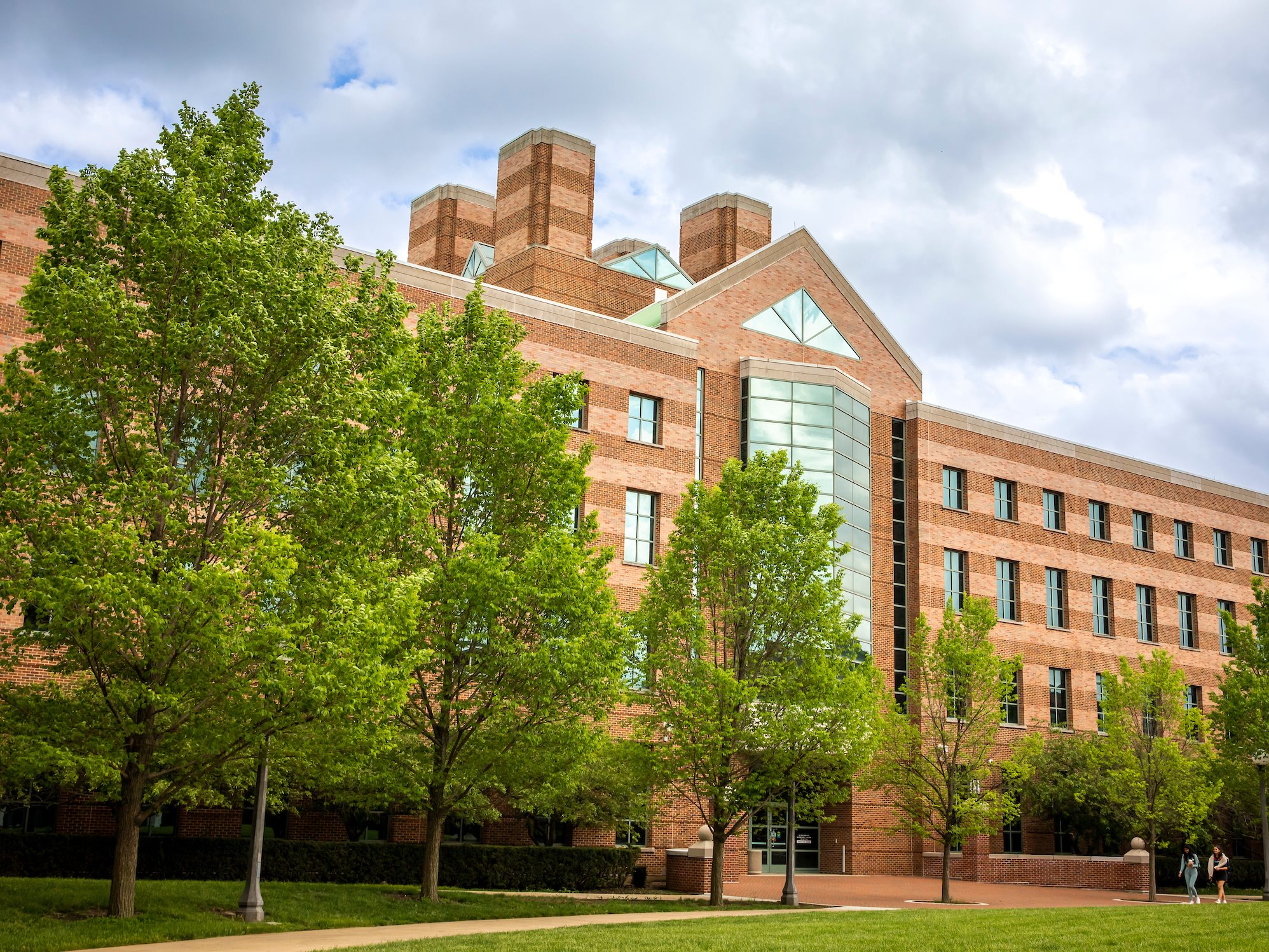 A white and red brick building with trees in front.