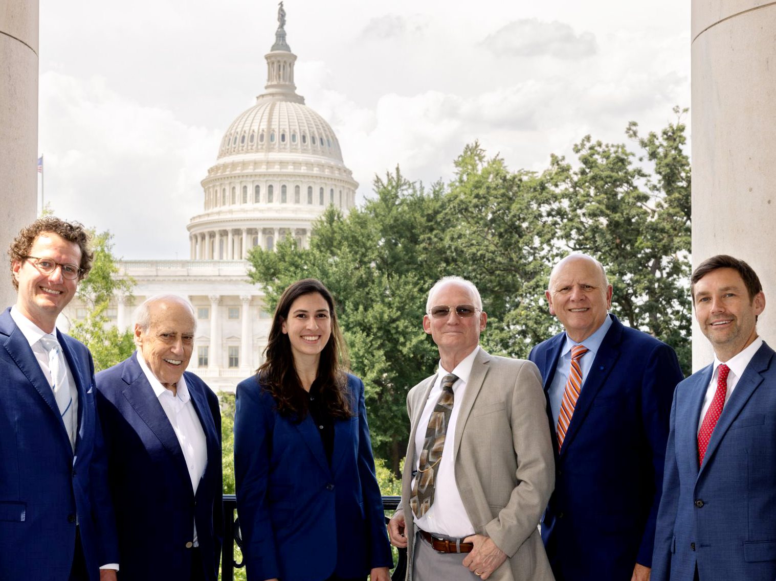 Six people stand in front of the Capitol dome, smiling.