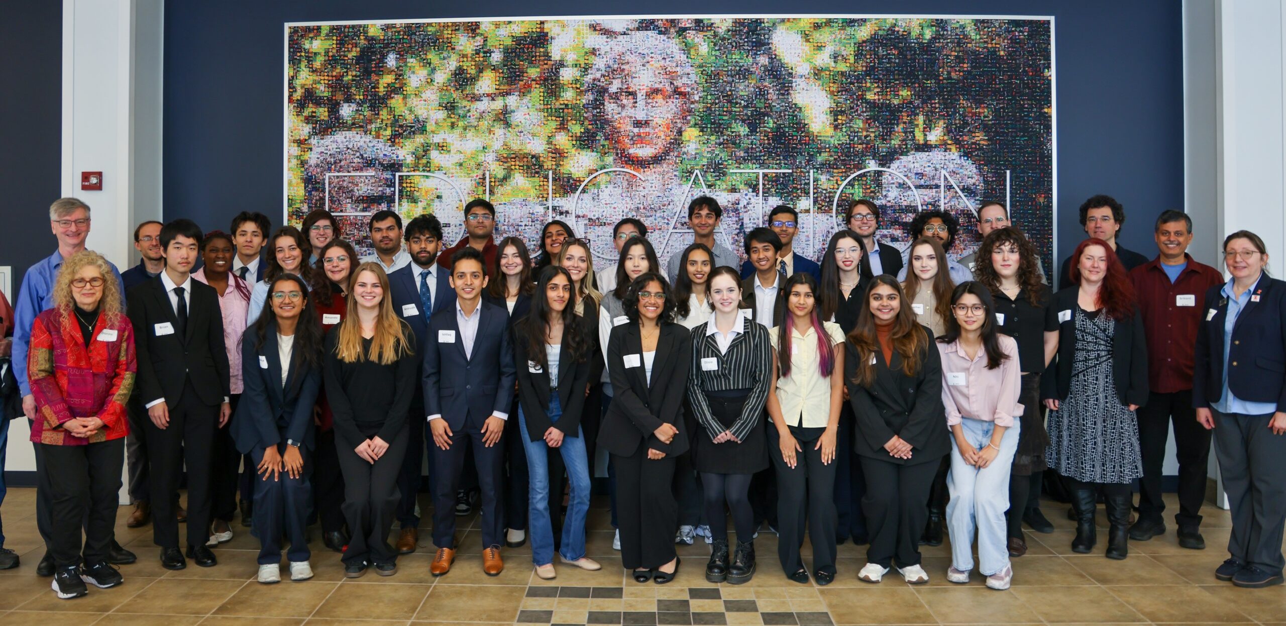 A large group of people stand in front of a photograph of Alma.