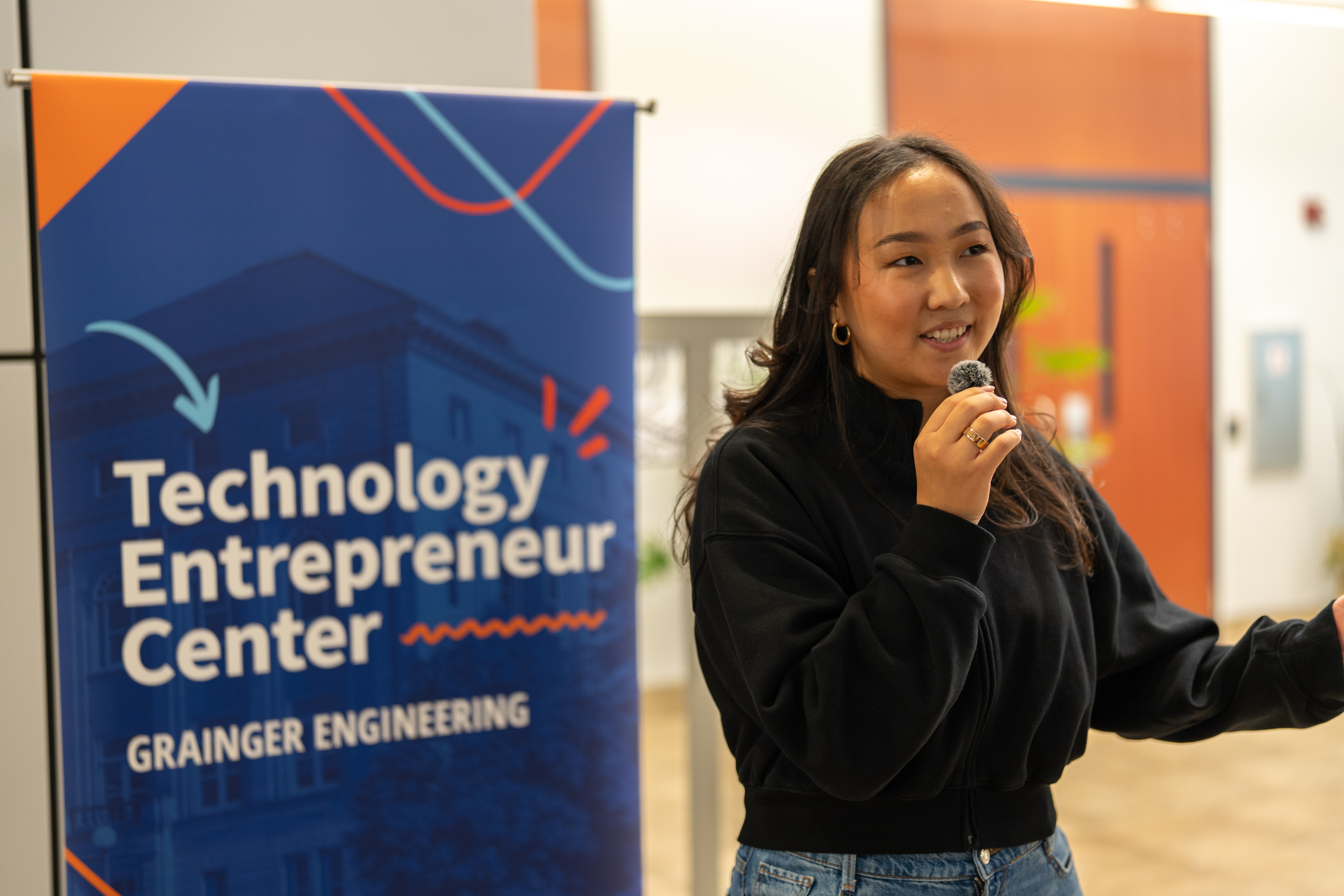 One person holds a mic and smiles in front of a banner