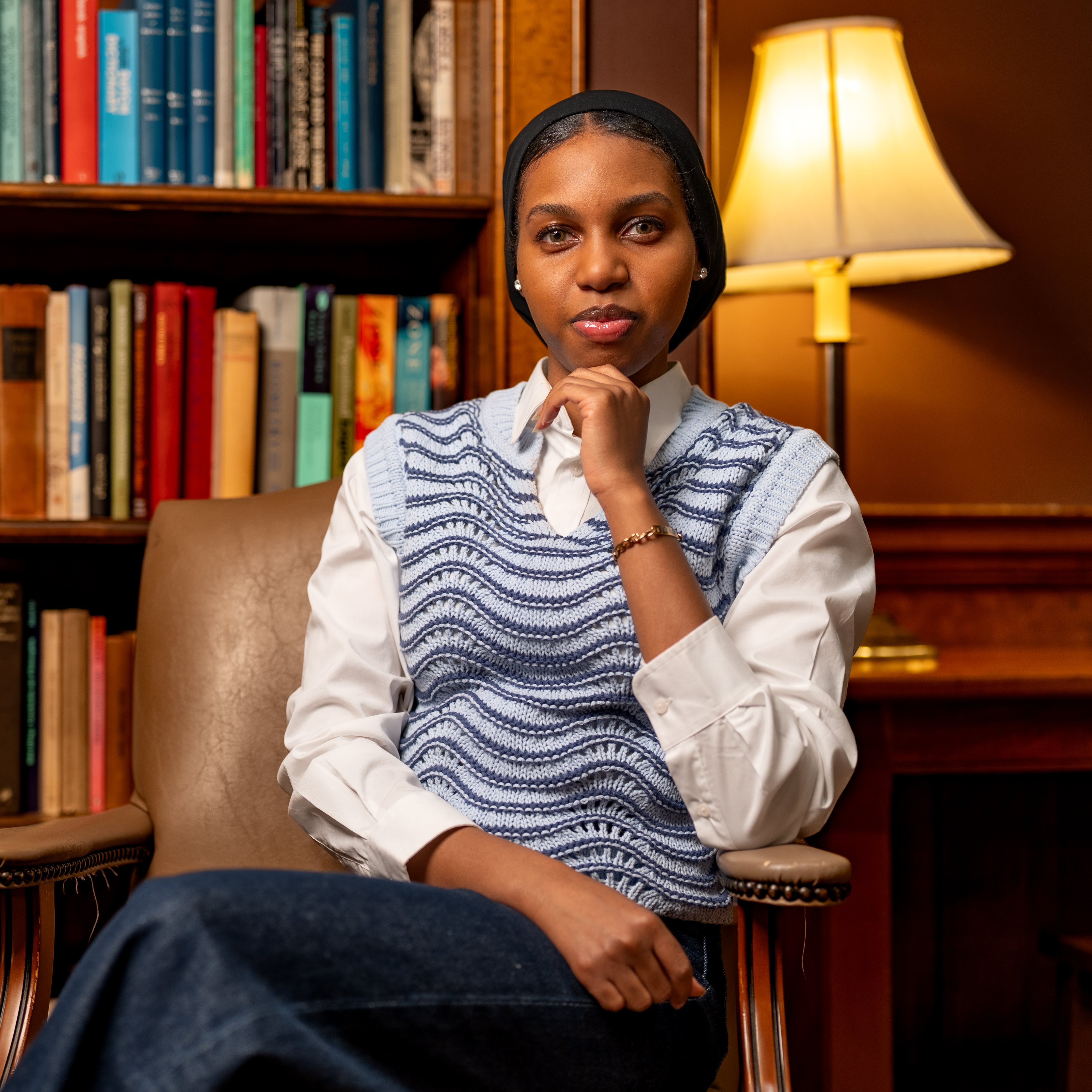 A woman sits in front of a stack of books and gestures.