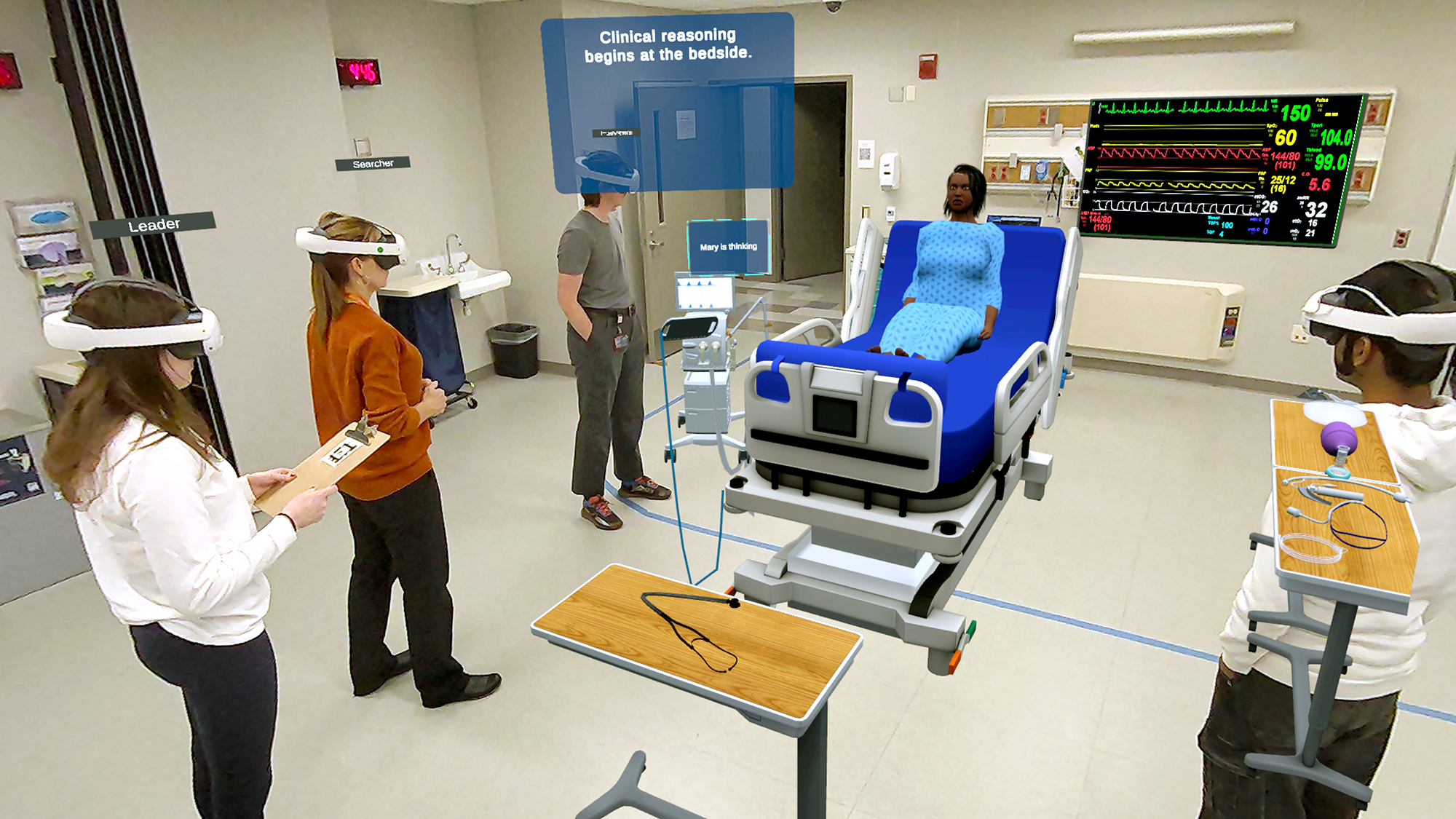 Four people in headsets at a hospital look at a simulation of a person in a medical bed with large feedback monitors on the walls.