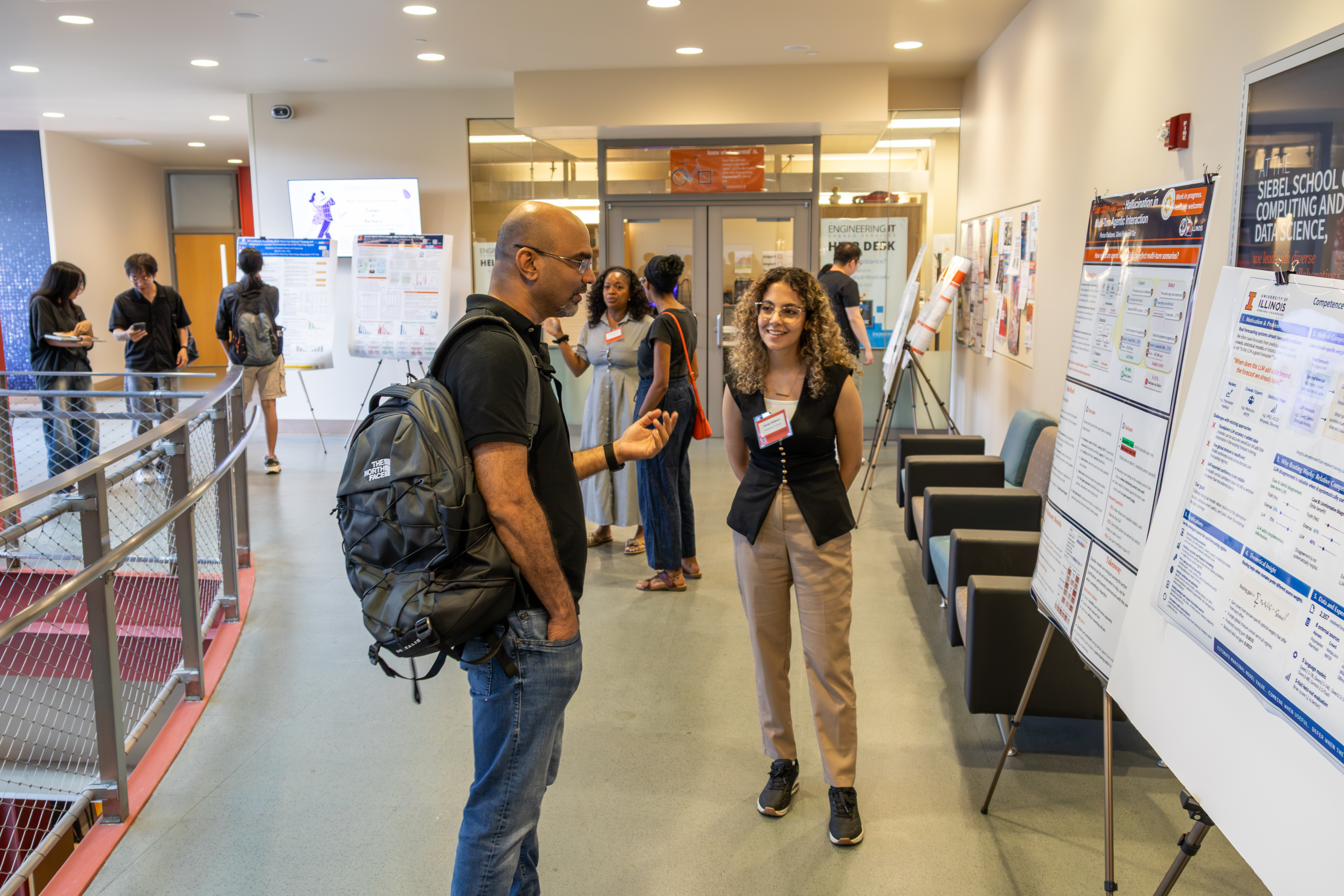 Two people in a hallway talking about a poster they are looking at