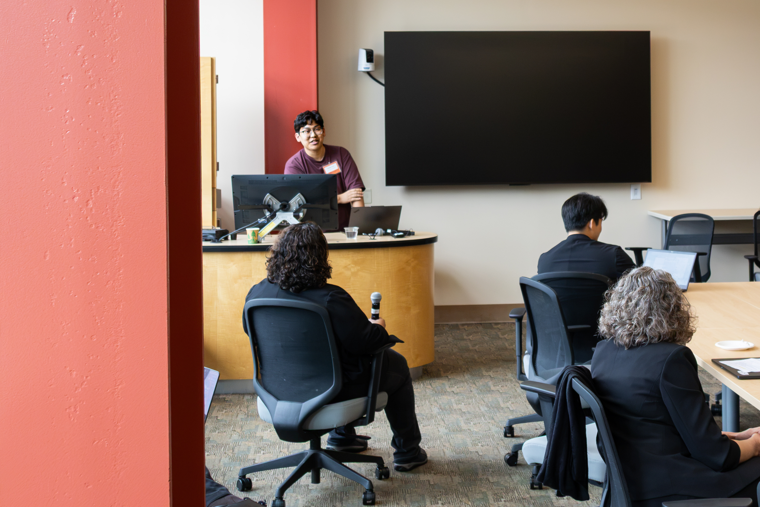A person stands behind a podium and talks to an audience sitting in chairs