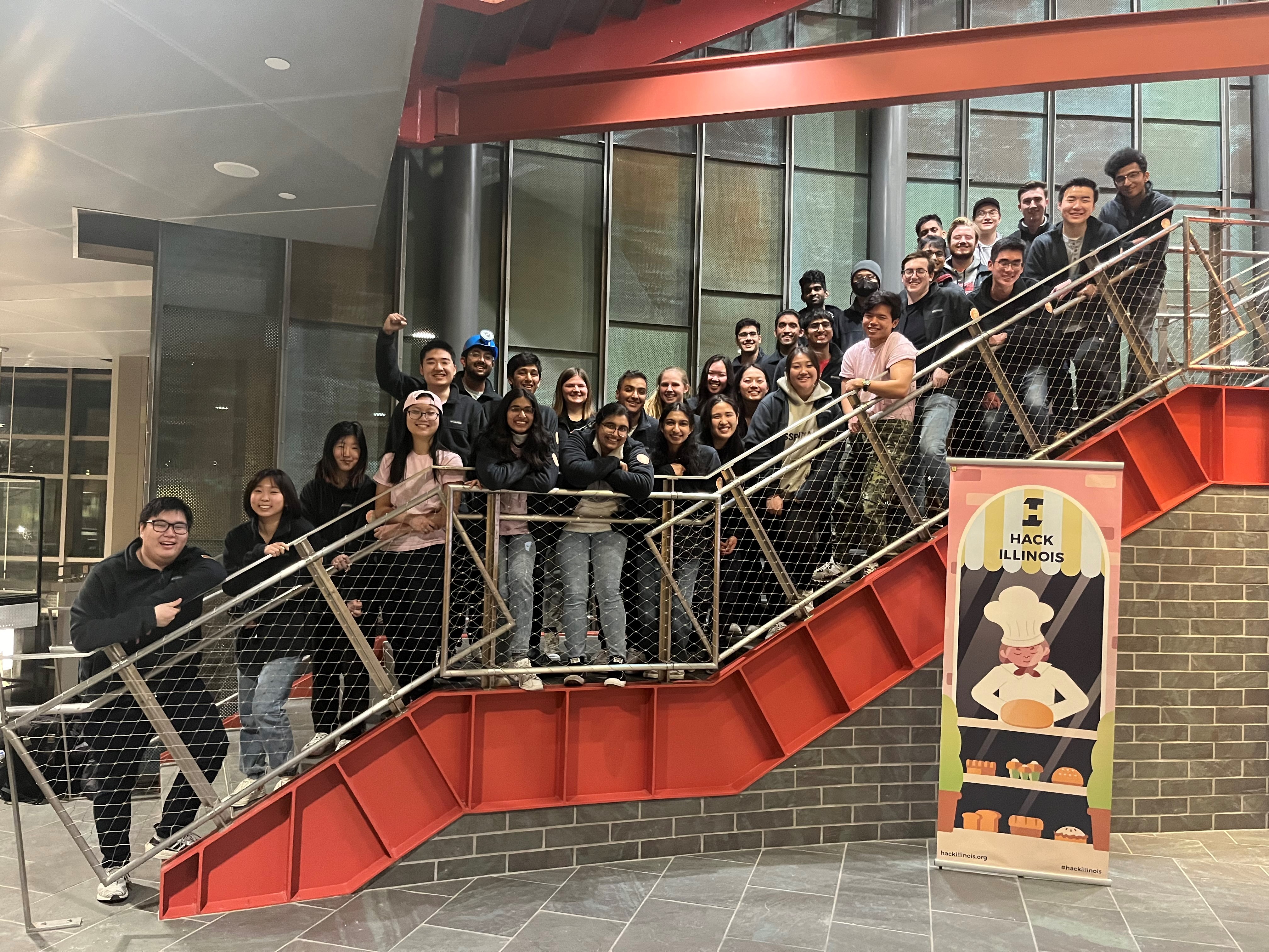 Several student members of the staff that hosted HackIllinois 2022, standing on a staircase in the Thomas M. Siebel Center for Computer Science.
