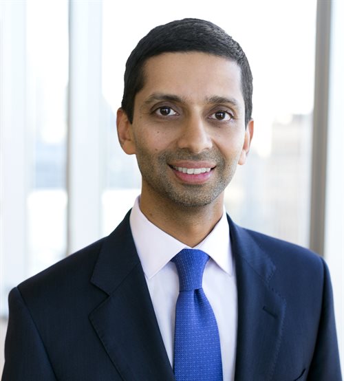 Portrait image of Umesh Subramanian in front of a business office window in a dark blue suit.