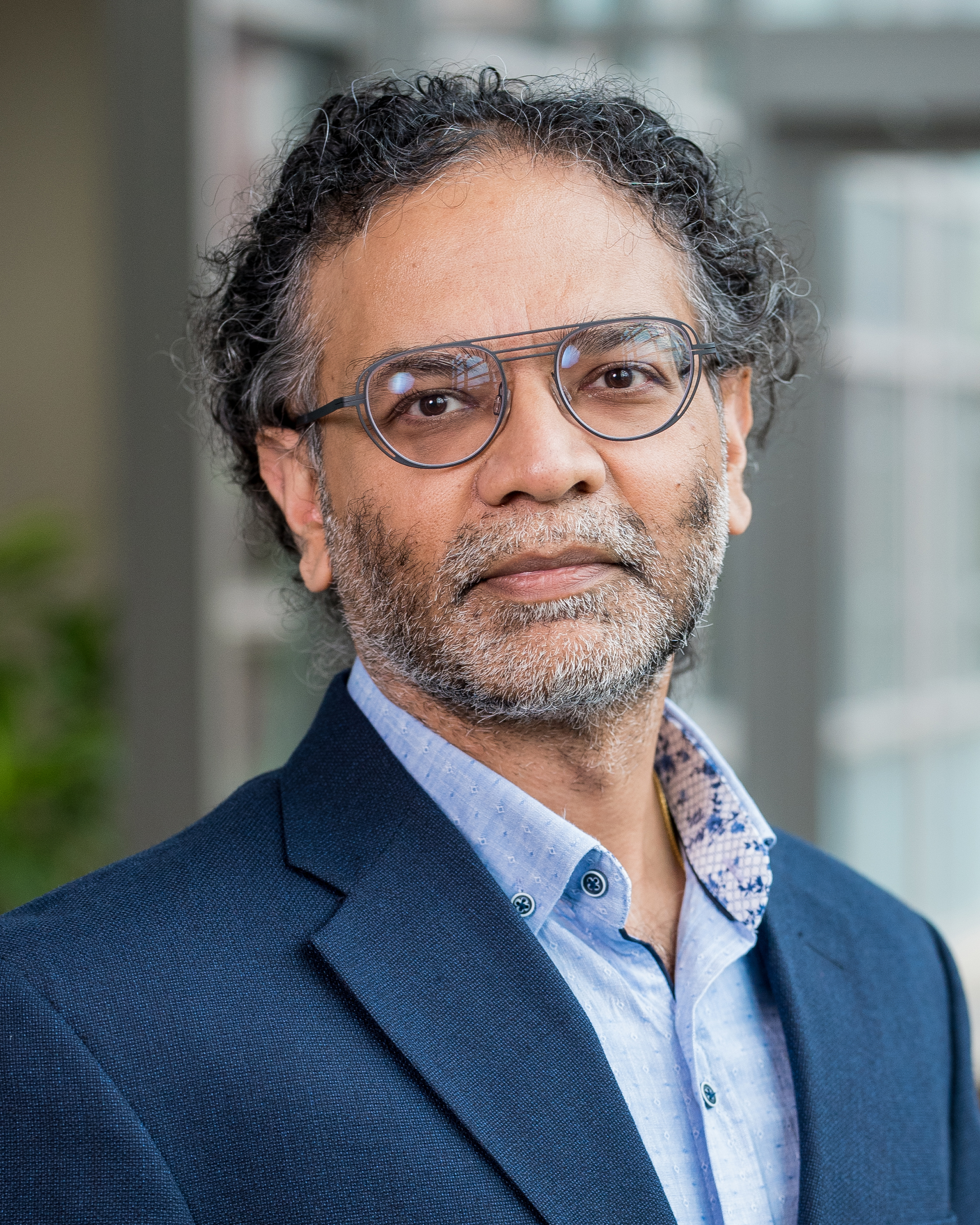 Illinois CS professor Indranil Gupta standing in front of a window in a blue shirt and glasses.