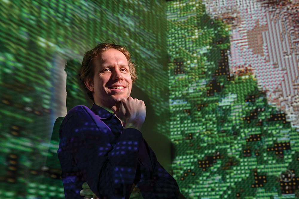 CS professor Wade Fagen Ulmschneider poses in front of a digital themed backdrop.