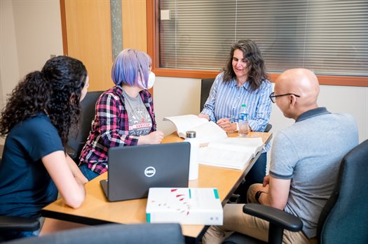 A woman sits at the head of the table teaching three students inside a classroom at the Siebel Center for Computer Science.