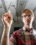 Zander Kelley at a clear whiteboard writing equations.