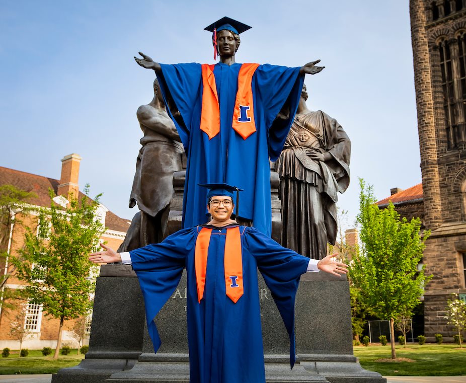 Illinois graduate fully dressed in cap and gown, preparing for graduation, poses in front of the Alma mater statue.