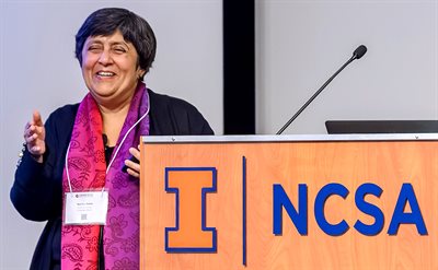 A woman at a podium gestures and smiles.