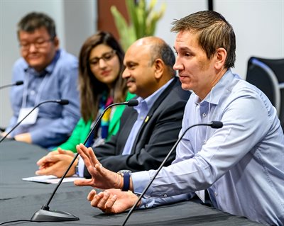 Four people sit at a table with microphones and interact with the audience.