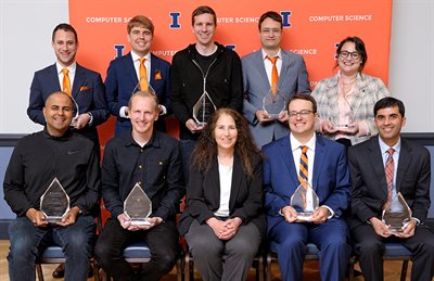 CS Alumni pose in front of an orange banner at the 2024 Computer Science Celebration of Excellence