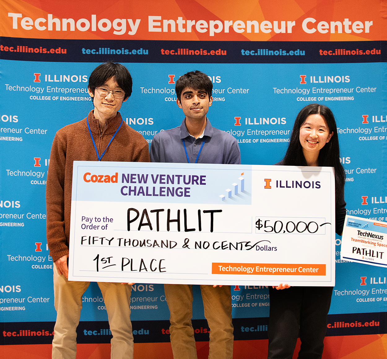 Three members of the Cozad New Venture Challenge 2024 Grand Prize winning team Pathlit  hold up a giant check.