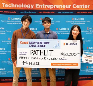 Three members of the grand prize winning team Pathlit of the Cozad New Venture Challenge 2024 hold up a huge check.