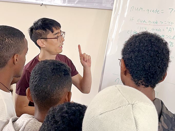 Daniel Kang explains a coding problem written on a whiteboard to a group of students at AddisCoder 2024.