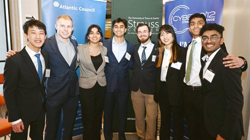 Eight people stand in front of banners with arms around each other's backs, smiling.