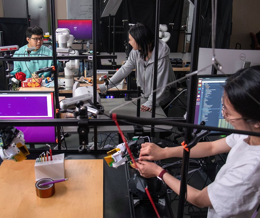 Three people work in a lab with robots and computer screens.